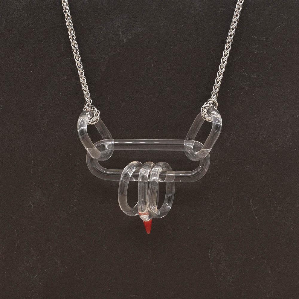 Necklace with long clear glass link and five smaller clear links. One smaller link has a red accent. Shown on a slate background.