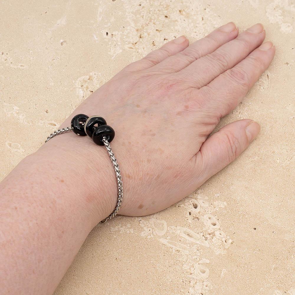 3 shiny black glass beads with big holes on a stainless steel chain bracelet, shown worn on a wrist.