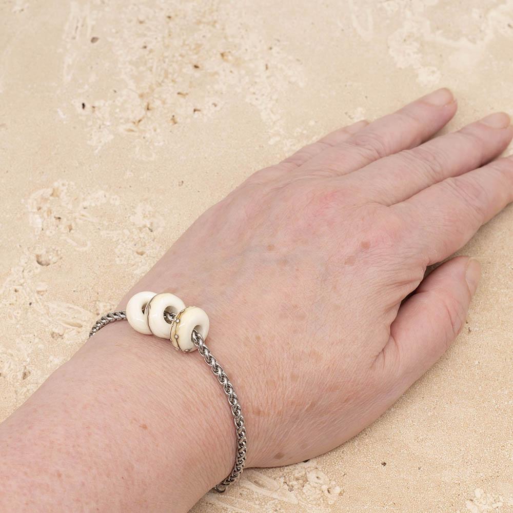 3 shiny ivory glass beads with big holes on a stainless steel chain bracelet, shown worn on a wrist.