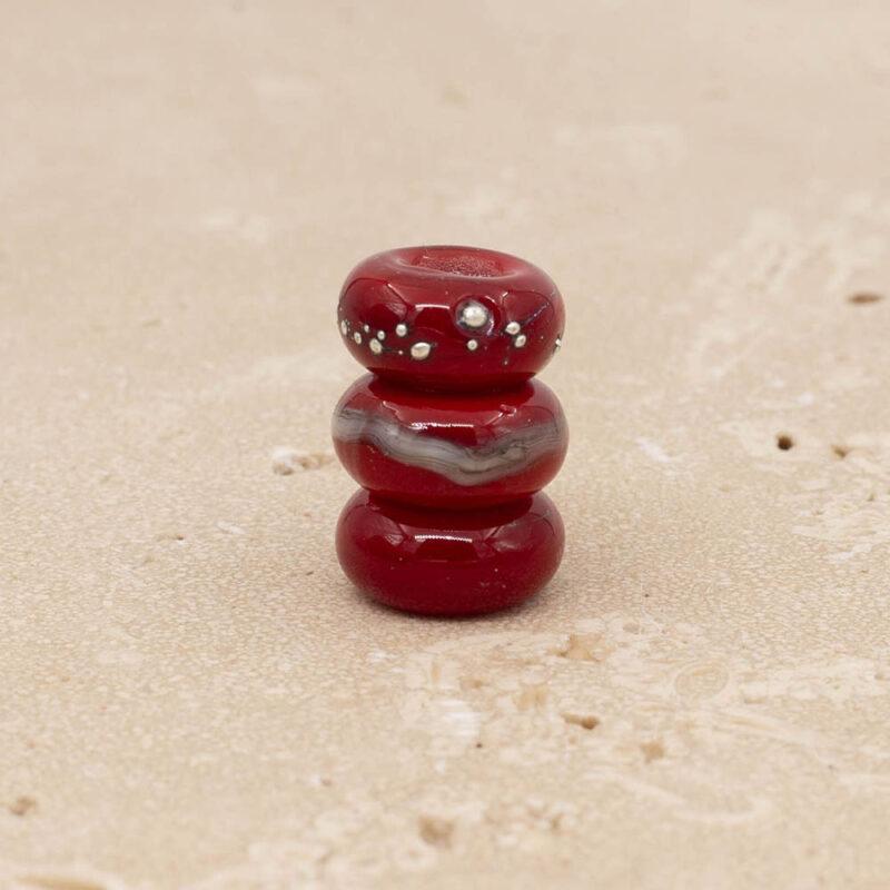 3 shiny red glass beads with big holes stacked on top of each other. One bead is plain, one has a band of silver and ivory glass and one has dots of silver.