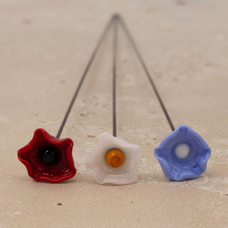 Close up top view of three bee sippers with ruffled edges. The colours are red with black centre, off white with yellow centre and periwinkle blue with white centre.