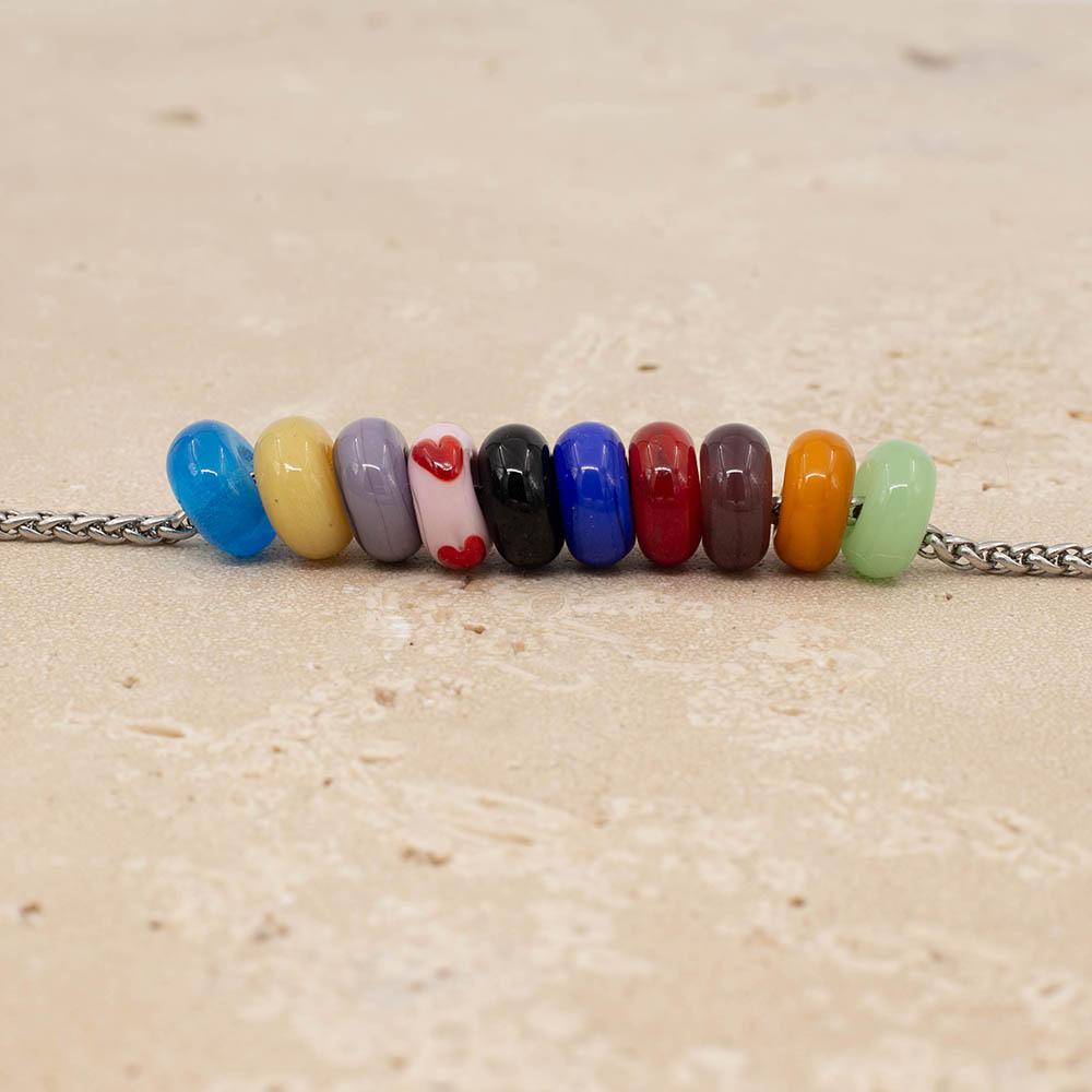 10 beads representing the Taylor Swift Eras Tour on a stainless steel chaiin. The colours are pale green, gold, deep purple, red, bright blue, black, pale pink with red hearts, lilac, pale yellow and bright turquoise.