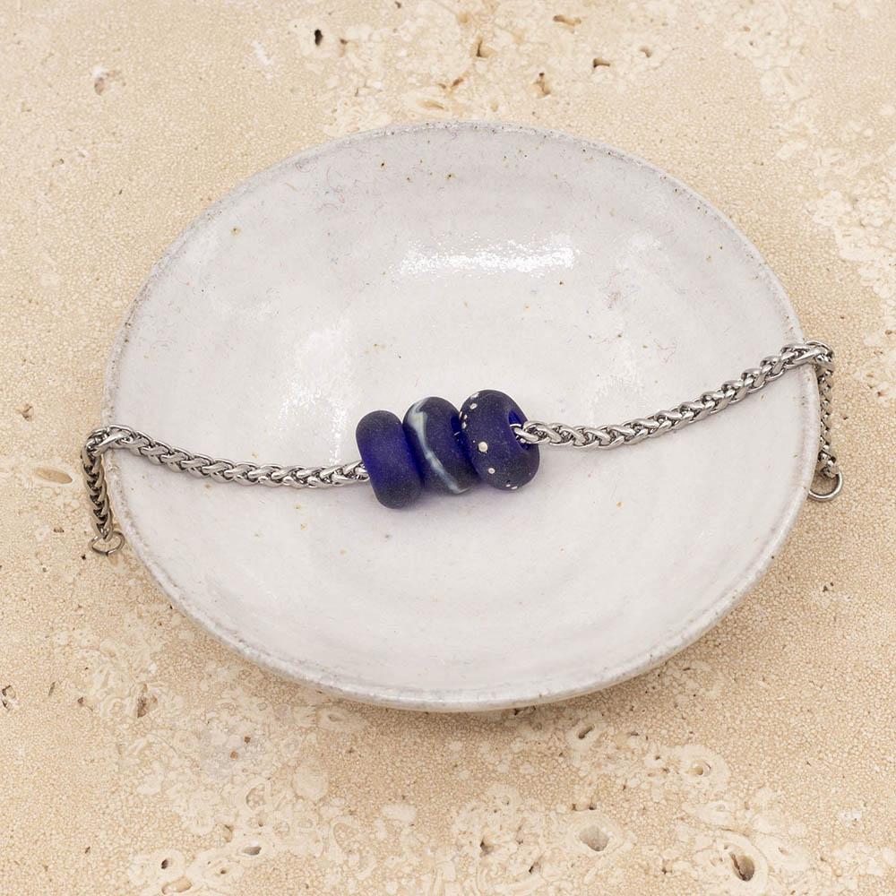 Close up of 3 frosted cobalt blue glass beads with big holes on a stainless steel chain sitting in a small white bowl.
