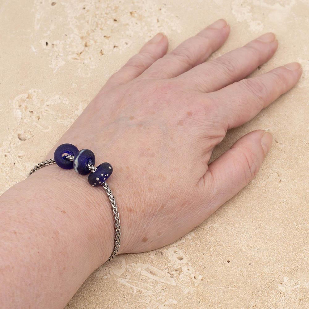 3 frosted cobalt blue glass beads with big holes on a stainless steel chain bracelet, shown worn on a wrist.
