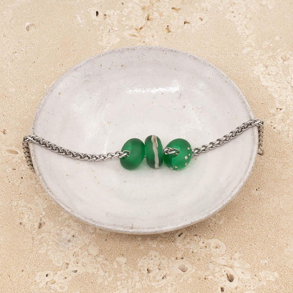 3 frosted green glass beads with big holes on a stainless steel chain sitting in a small white bowl.