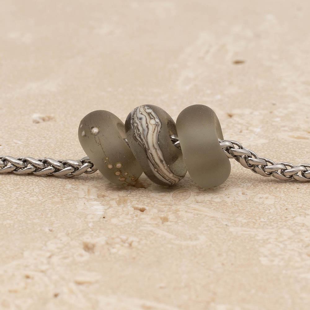 Close up of 3 frosted grey glass beads with big holes on a stainless steel chain.