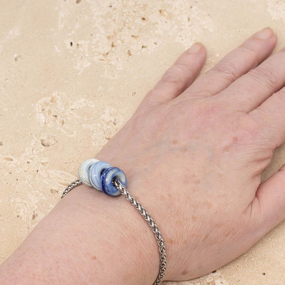 3 frosted ivory and blue glass beads with big holes on a stainless steel chain bracelet, shown worn on a wrist.