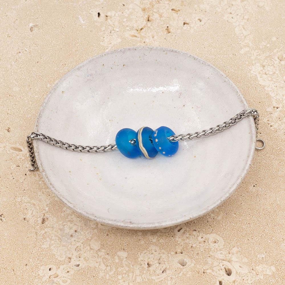 3 decorated frosted turquoise glass beads with big holes on a stainless steel chain sitting in a small white dish.