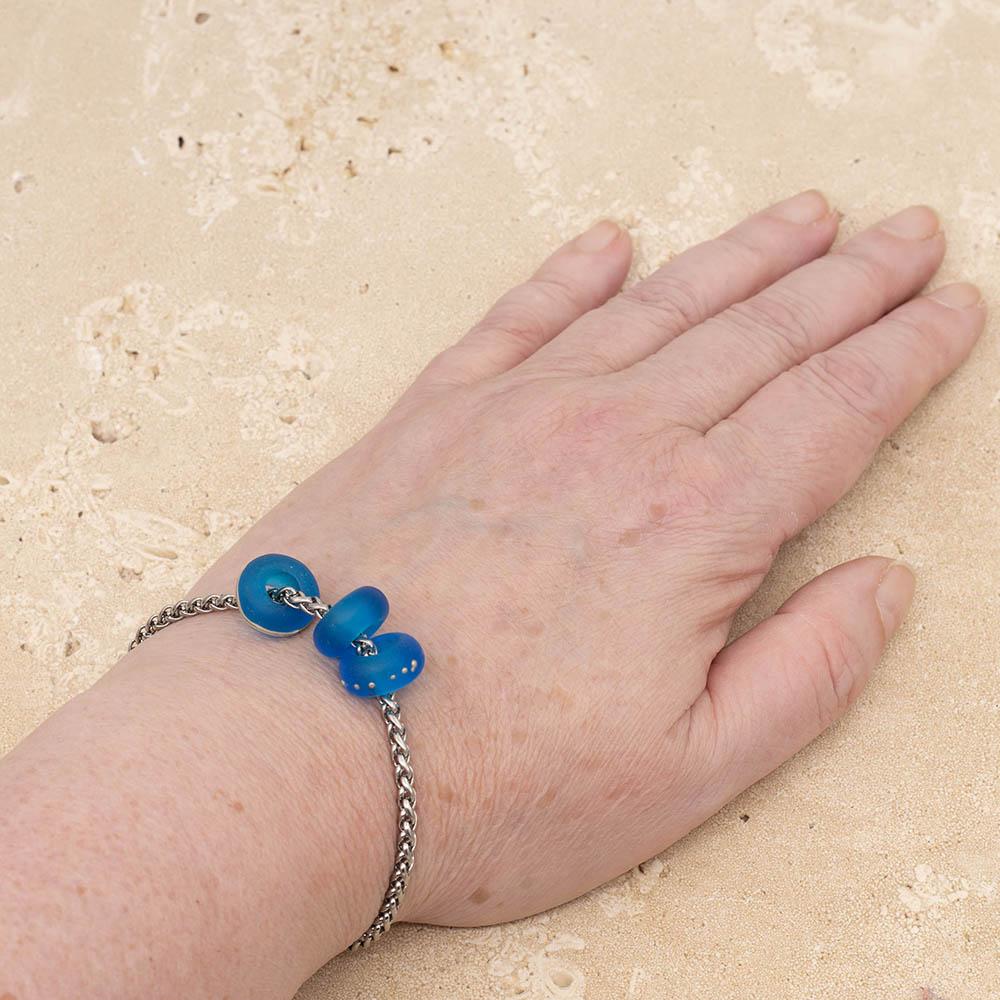3 decorated frosted turquoise glass beads with big holes on a bracelet, shown on a wrist.