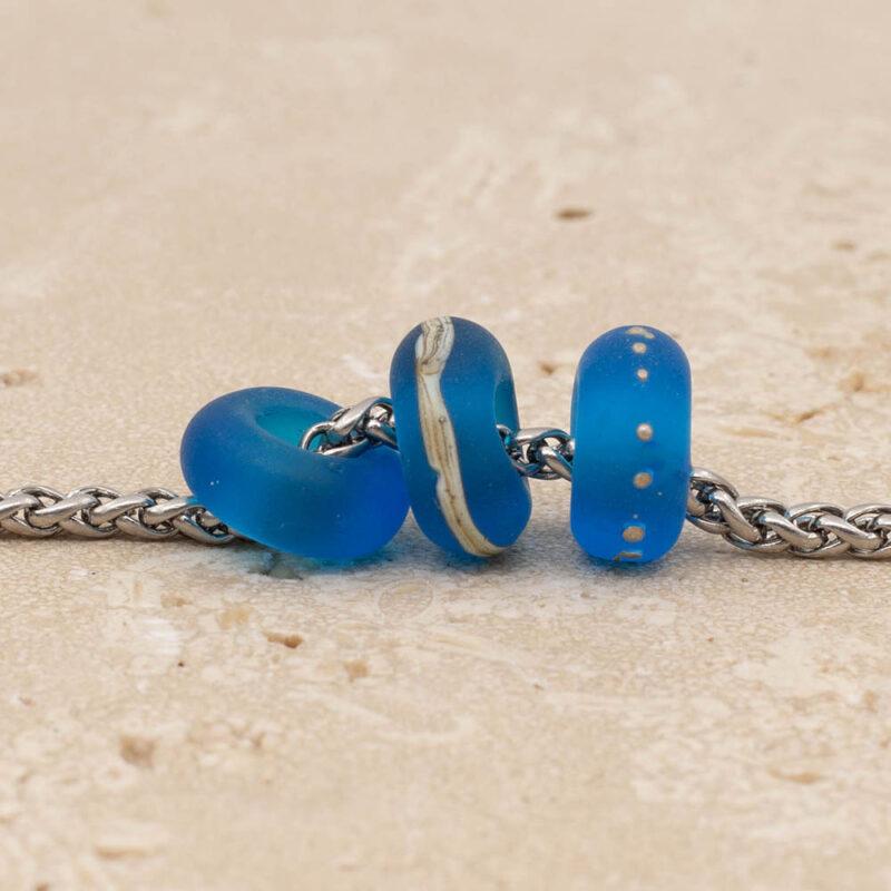 Close up of 3 decorated frosted turquoise glass beads with big holes on a stainless steel chain.