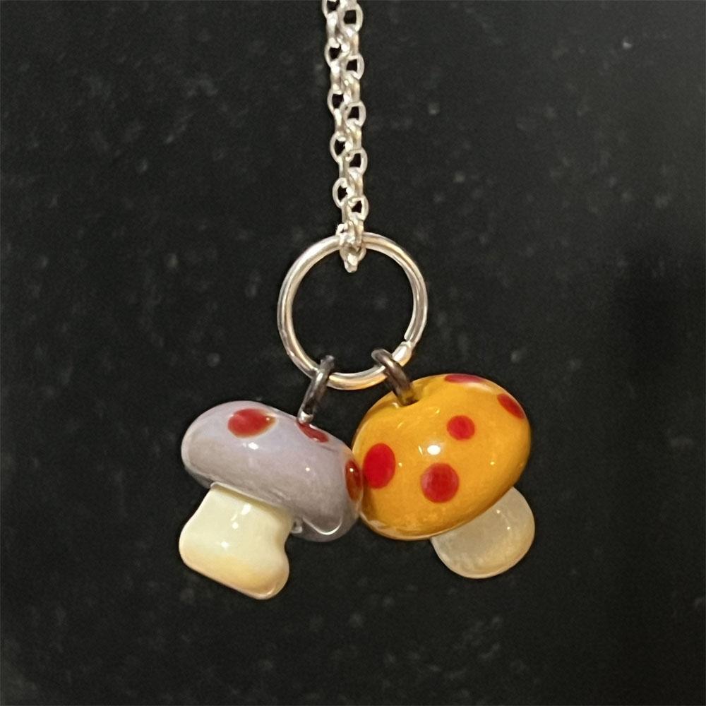 Double mushroom charm with purple and golden yellow toped mushrooms with red dots on a sterling silver chain.