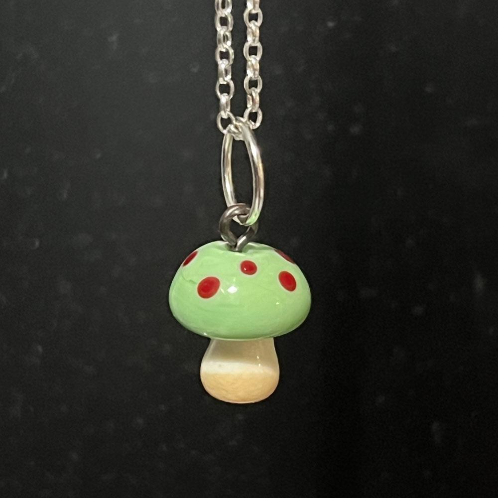 Mushroom charm with green top and red dots on a sterling silver chain.