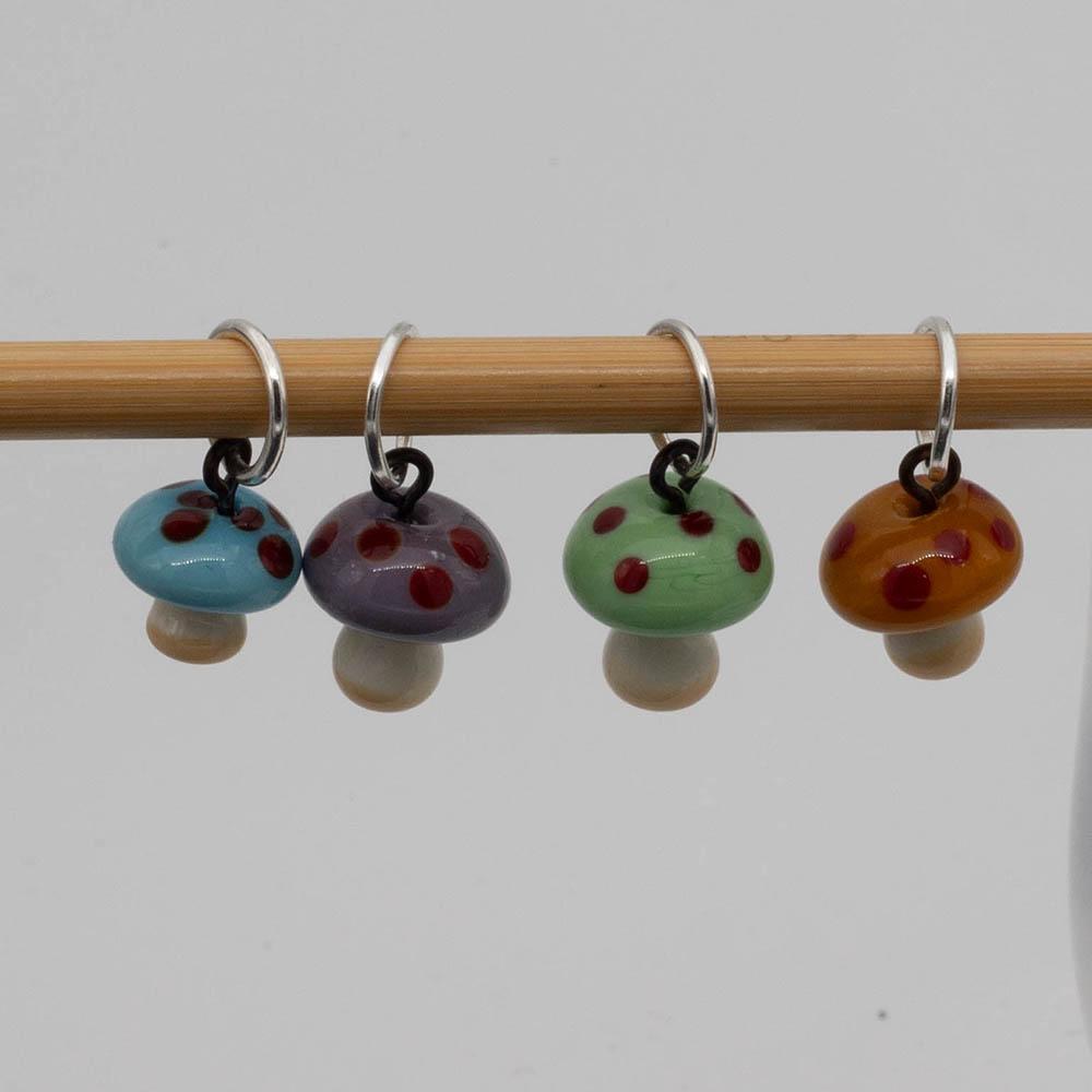 mushroom stitch markers. The mushrooms are golden yellow, green,turquoise and purple and all four have red dots