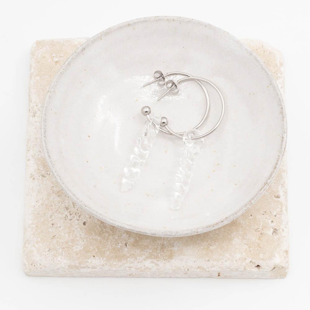two small clear icicle glass icicles on round earring hoops with butterfly backs sit in a small ceramic bowl