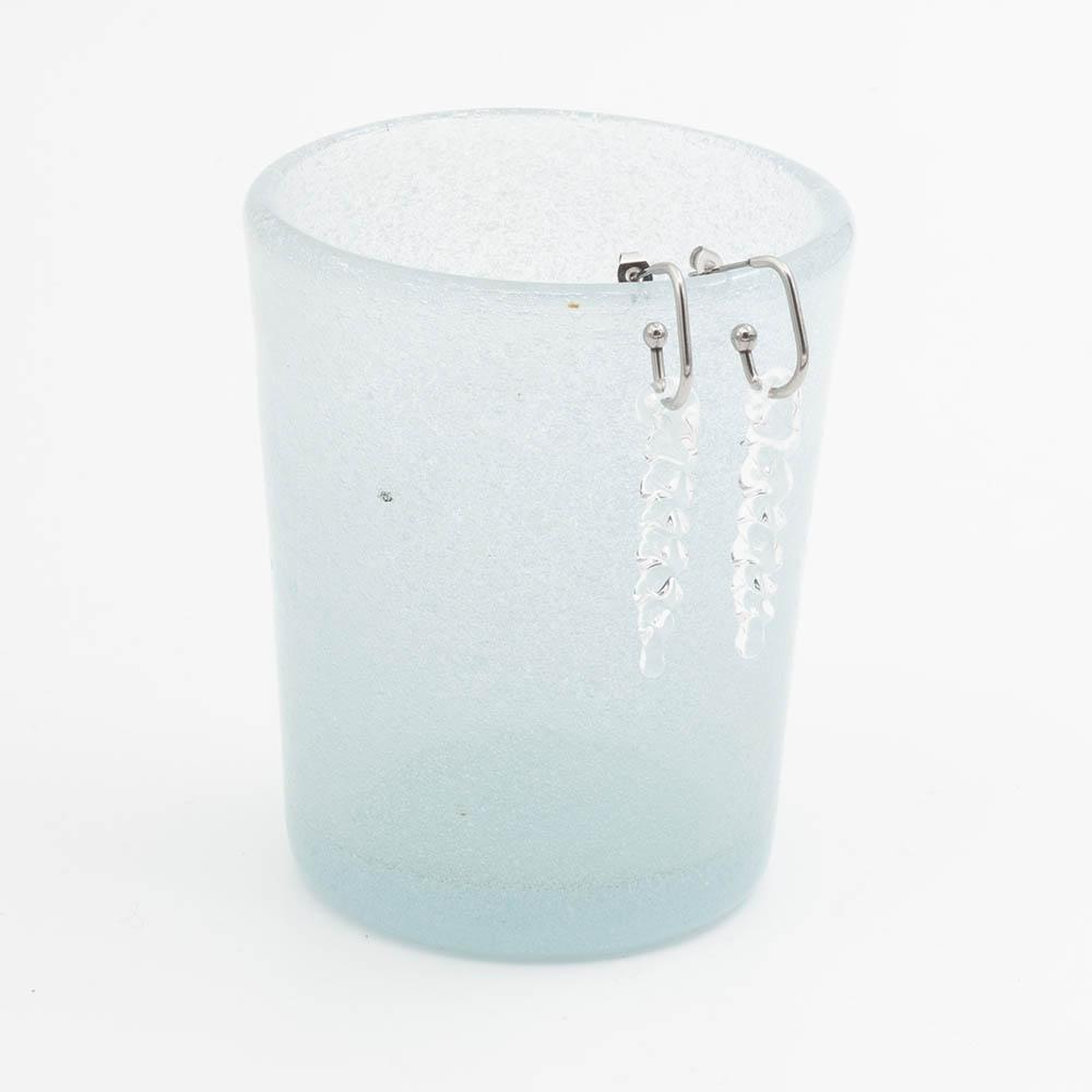 two large clear icicle glass icicles on oval earring hoops hang on the edge of a frosted blue tumbler