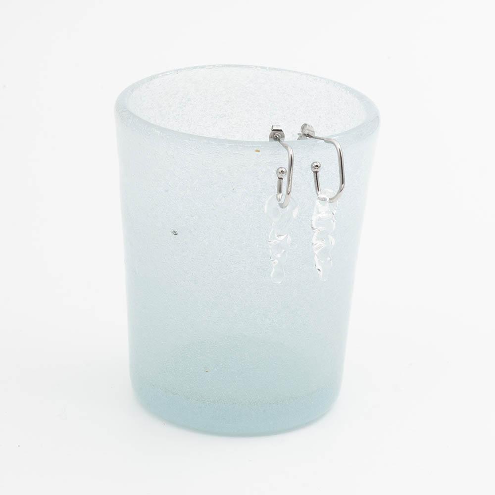 two small clear icicle glass icicles on oval earring hoops hang on the edge of a frosted blue tumbler
